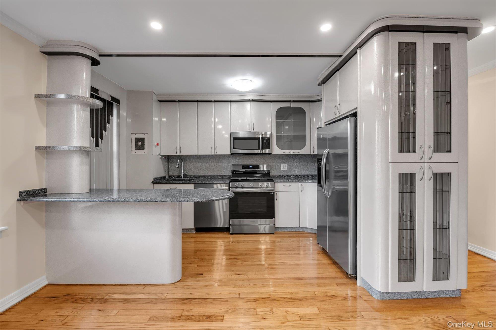65-35 Yellowstone Boulevard, Unit 4G Queens, NY 11375 - Photo 5 of 10 Kitchen with glass insert cabinets, stainless steel appliances, white cabinets, light wood-style floors, and a peninsula