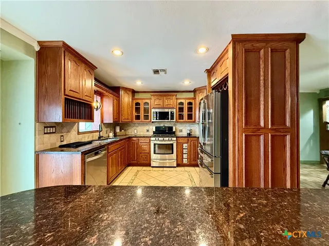 a kitchen with stainless steel appliances granite countertop a refrigerator a stove and a sink with wooden floor