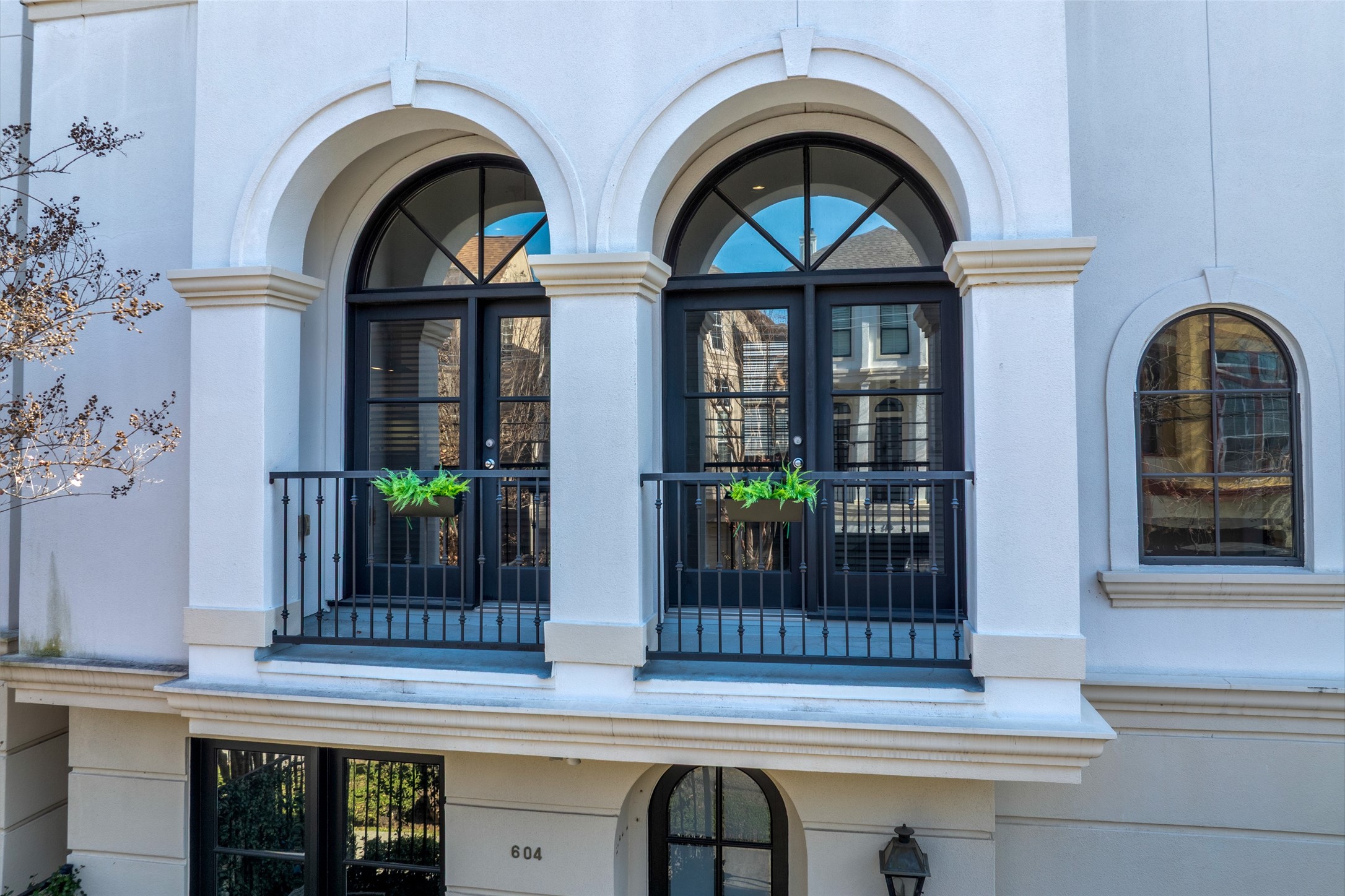 604 Knox Street Houston, TX 77007 - Photo 2 of 42 Elegant home exterior featuring two large arched windows with black frames, a small balcony adorned with green plants, and a clean, light-colored facade that exudes a modern yet classic vibe.