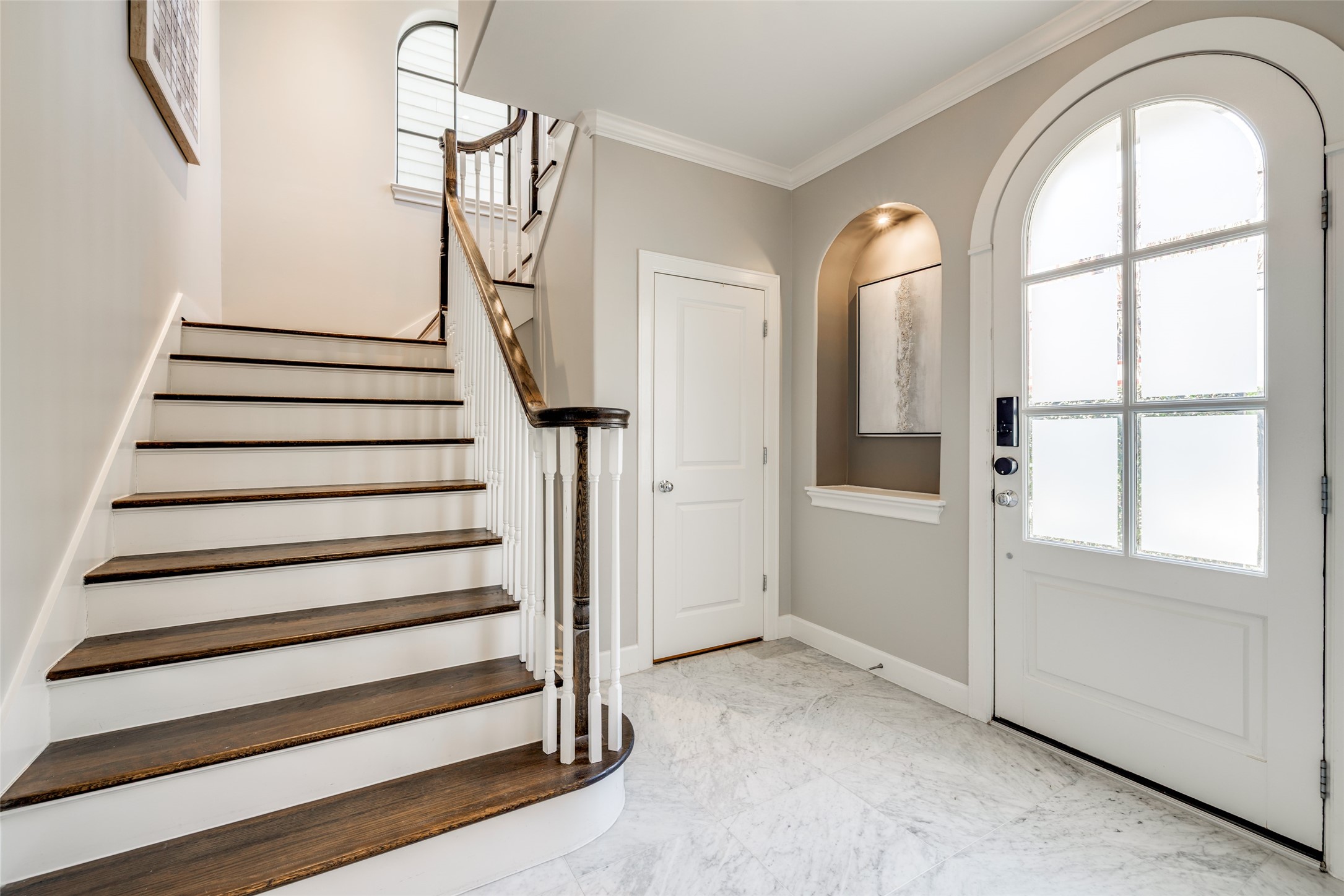 604 Knox Street Houston, TX 77007 - Photo 3 of 42 This entryway features elegant marble flooring, a wooden staircase with white risers, and a stylish arched front door with frosted glass panels. The neutral wall tones and decorative niche add a sophisticated touch.