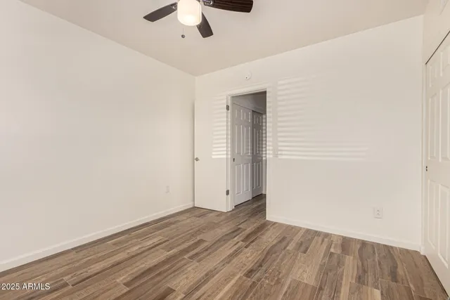 an empty room with wooden floor chandelier fan and windows