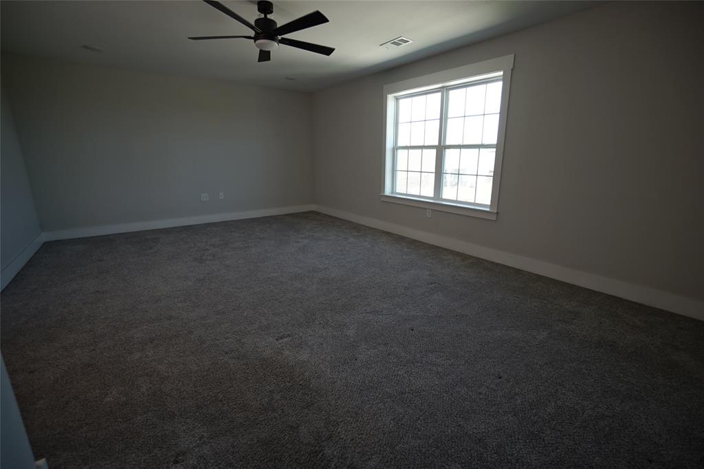 1764 Palladio Loop Princeton, TX 75407 - Photo 29 of 40 Spacious room featuring neutral wall tones, grey carpet, a large window with white trim, and a ceiling fan with integrated lighting