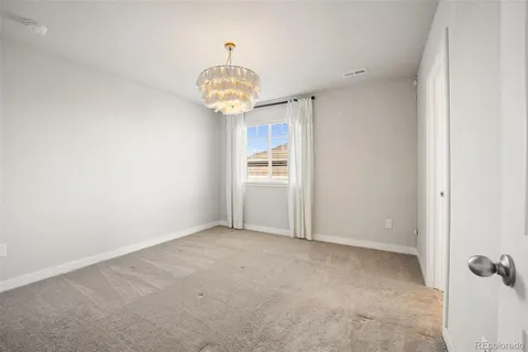 an empty room with a chandelier fan and kitchen view