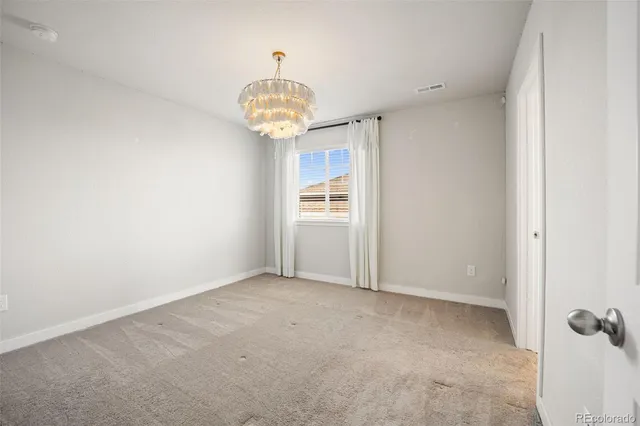 an empty room with a chandelier fan and kitchen view