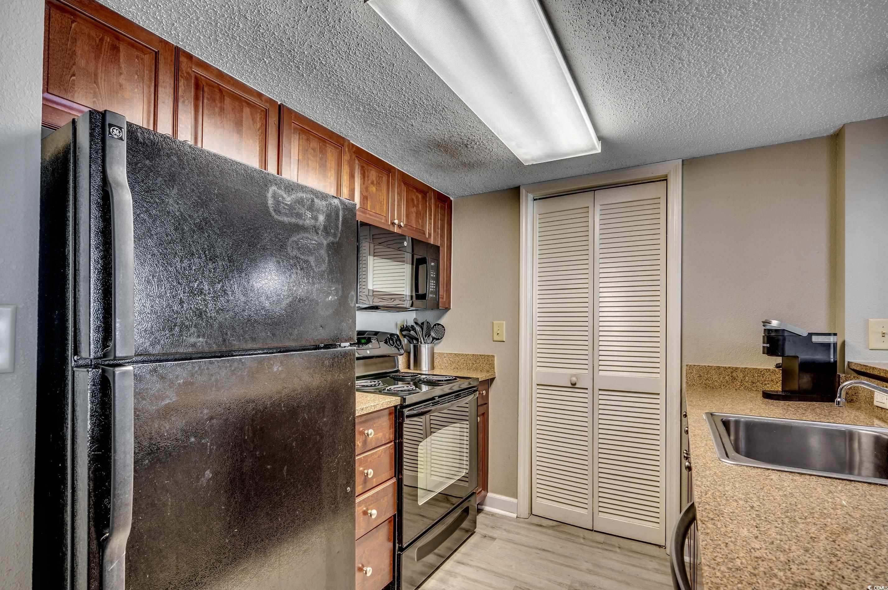 5200 North Ocean Boulevard, Unit 1037 Myrtle Beach, SC 29577 - Photo 12 of 40 Kitchen with black appliances, light wood-style floors, a textured ceiling, brown cabinets, and light stone countertops