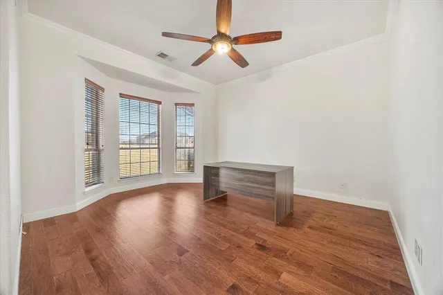 an empty room with wooden floor chandelier fan and windows