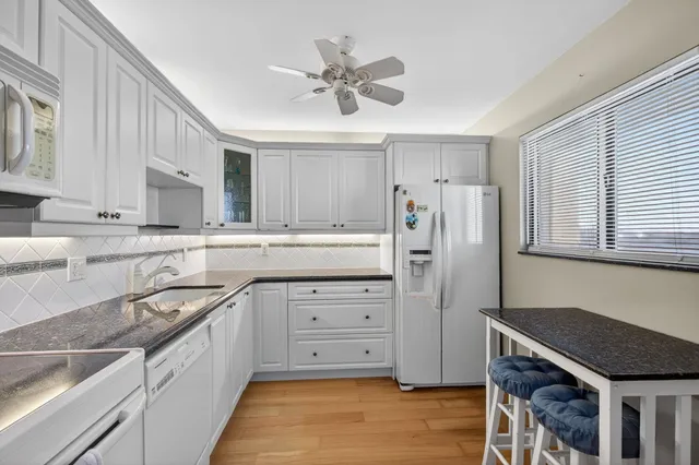 a kitchen with stainless steel appliances granite countertop a refrigerator a sink dishwasher a stove and white countertops with wooden floor