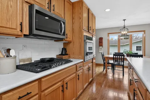 a kitchen with stainless steel appliances kitchen island granite countertop a stove a sink a dining table and chairs with wooden floor