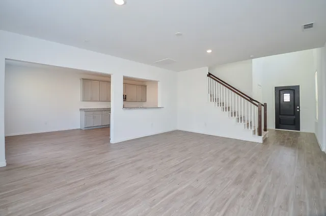 a view of an empty room with wooden floor and a kitchen