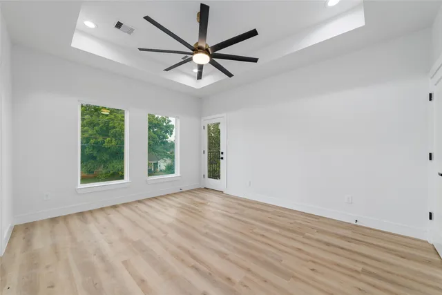 an empty room with wooden floor fan and windows