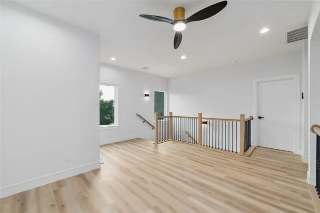an empty room with wooden floor fan and windows