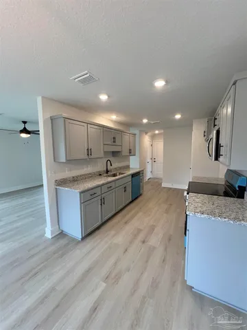 a large kitchen with a large counter top a sink stainless steel appliances and cabinets