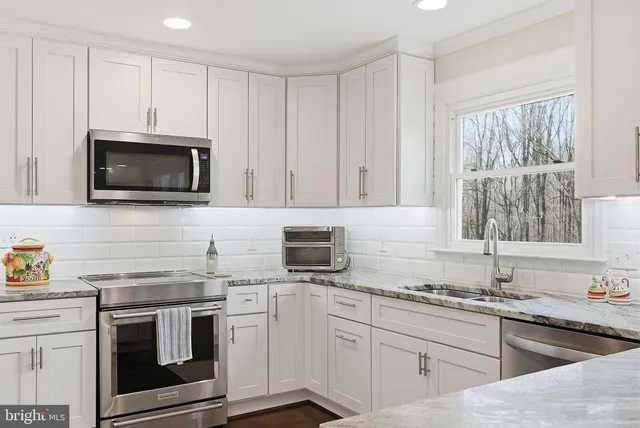 a kitchen with stainless steel appliances granite countertop white cabinets a sink a stove a microwave and wooden floors