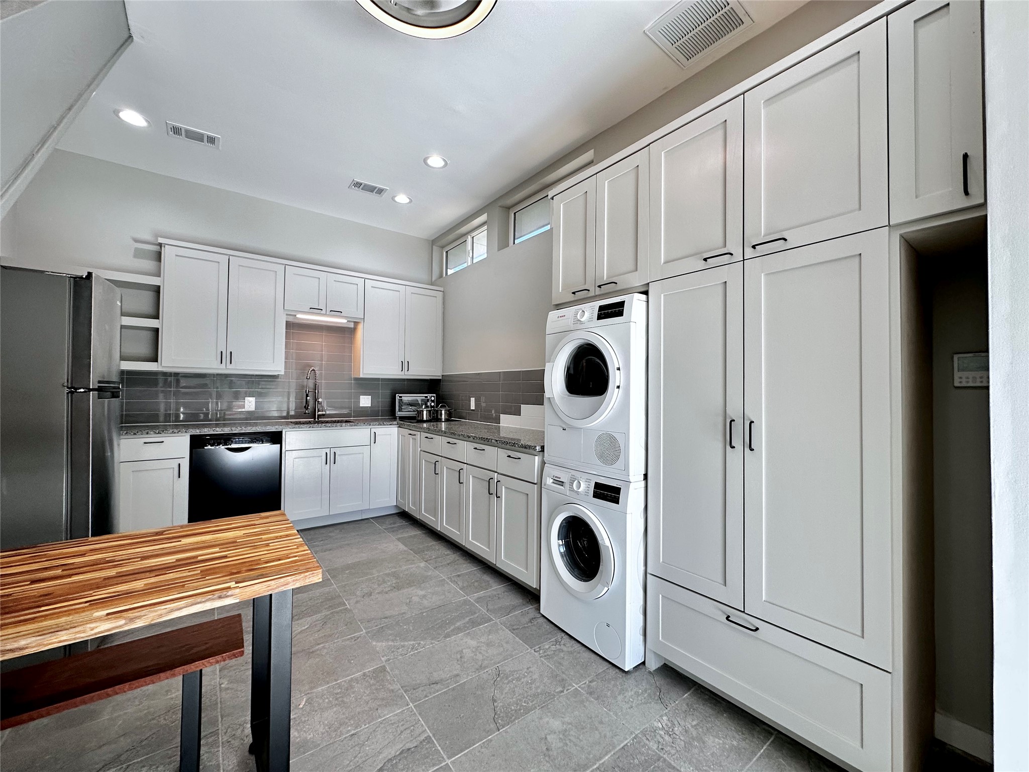 914 East 39th Street, Unit 2 Austin, TX 78751 - Photo 6 of 34 Kitchen with white cabinets, freestanding refrigerator, stacked washer and clothes dryer, stone tile flooring, and dishwasher