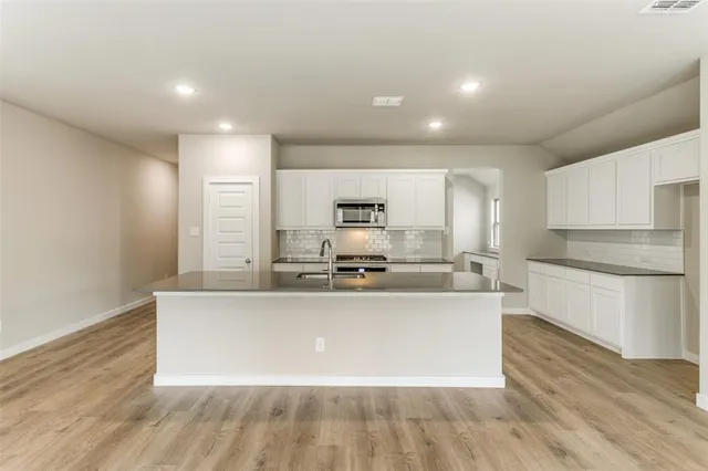 a large kitchen with stainless steel appliances a large counter top a stove and white cabinets