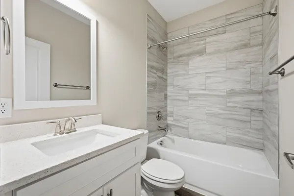 a bathroom with a granite countertop bathtub shower sink vanity mirror and toilet
