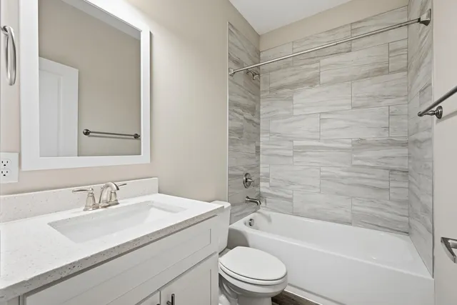 a bathroom with a granite countertop bathtub shower sink vanity mirror and toilet