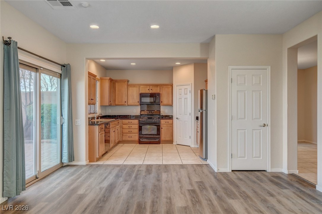 2460 Rue Bienville Way Henderson, NV 89044 - Photo 12 of 50 Kitchen with dark countertops, black appliances, light brown cabinets, light wood-type flooring, and recessed lighting