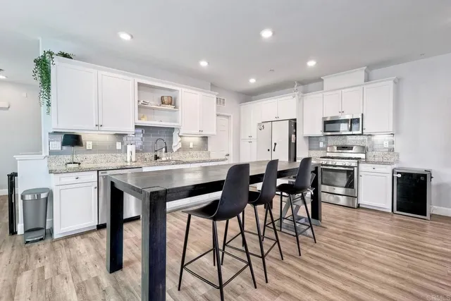 a kitchen with stainless steel appliances granite countertop a stove a sink a microwave a refrigerator and white cabinets with wooden floor