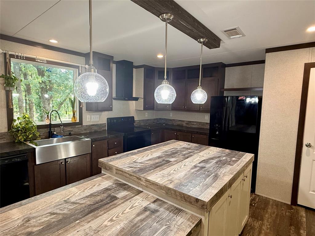 145 Adalida Lane Springtown, TX 76082 - Photo 9 of 29 Kitchen featuring a multi-level island with wood-finish countertop, stainless steel farmhouse sink, pendant lighting, dark wood cabinetry, and black appliances