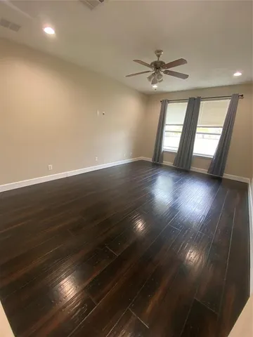 an empty room with wooden floor fan and windows