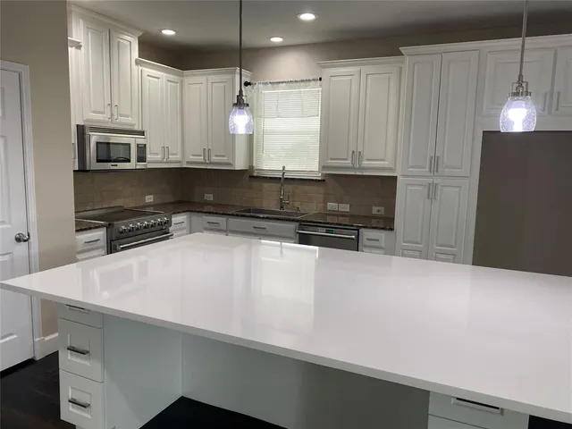 a kitchen with stainless steel appliances a sink a stove a refrigerator and white cabinets