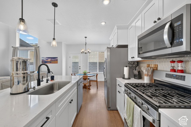 4751 Heartwood Road Mapleton, UT 84664 - Photo 11 of 33 White cabinetry, stainless steel appliances, wood-finish flooring, island with integrated sink, and pendant lighting