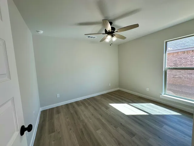 an empty room with wooden floor fan and windows