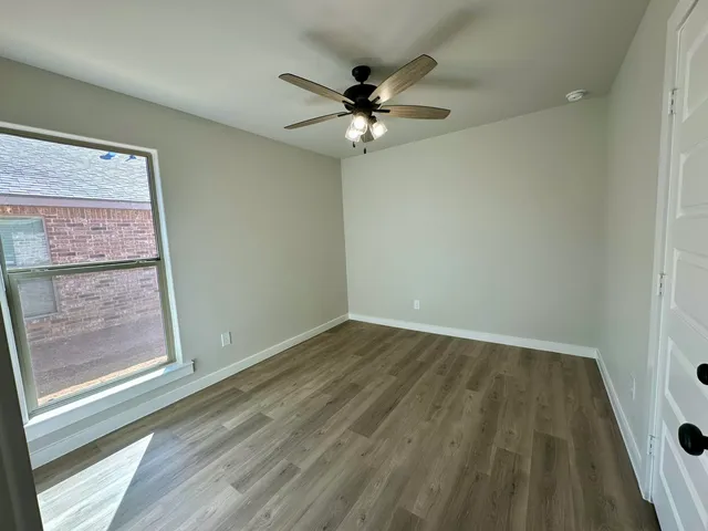 an empty room with wooden floor fan and windows