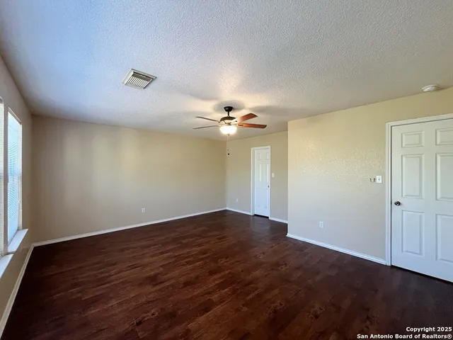 an empty room with wooden floor chandelier fan and windows