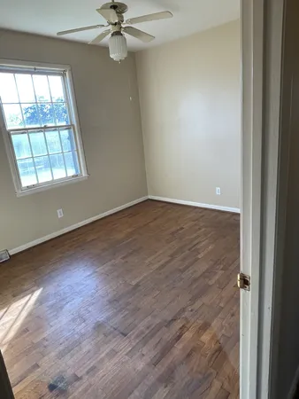 an empty room with wooden floor fan and windows