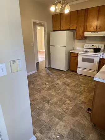 a view of a refrigerator in kitchen and an empty room with wooden floor