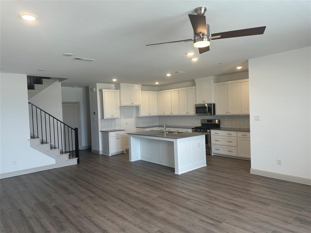 a large kitchen with a large counter top a sink stainless steel appliances and cabinets