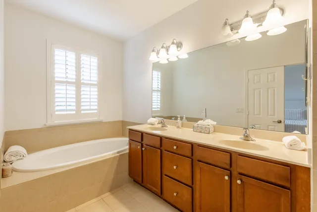 a bathroom with a tub a double vanity sink a window a mirror and a bathtub