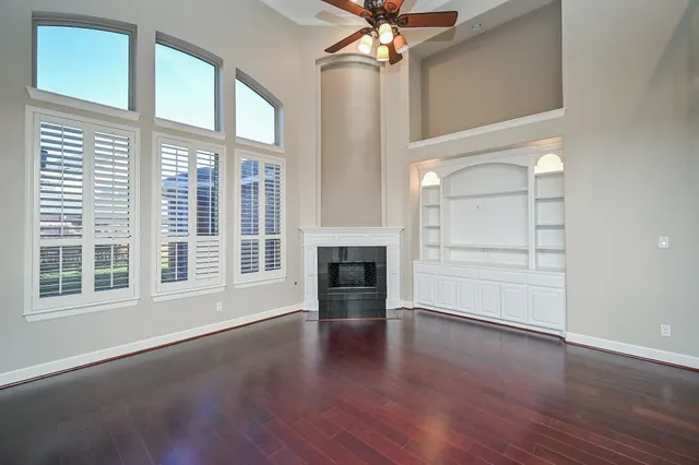 an empty room with wooden floor fireplace and windows