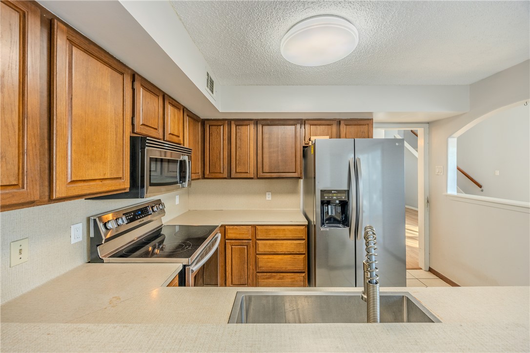 2002 South Lubbock Street Brenham, TX 77833 - Photo 11 of 26 Kitchen with light countertops, stainless steel appliances, brown cabinetry, and a textured ceiling