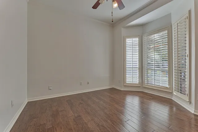 an empty room with wooden floor chandelier fan and windows