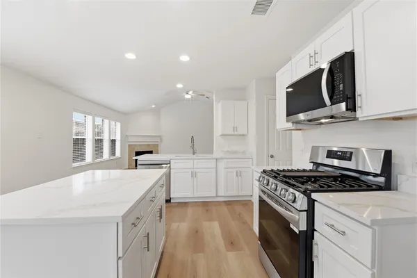 a kitchen with stainless steel appliances granite countertop a stove top oven a sink dishwasher and white cabinets with wooden floor