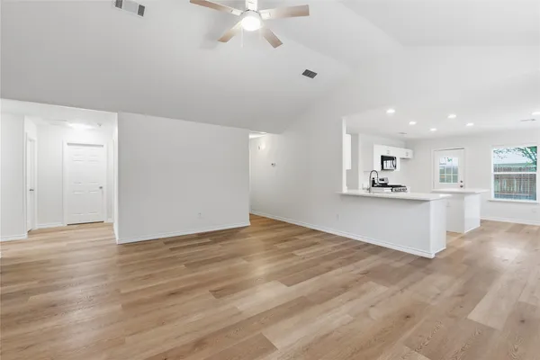 a view of an empty room with wooden floor and kitchen