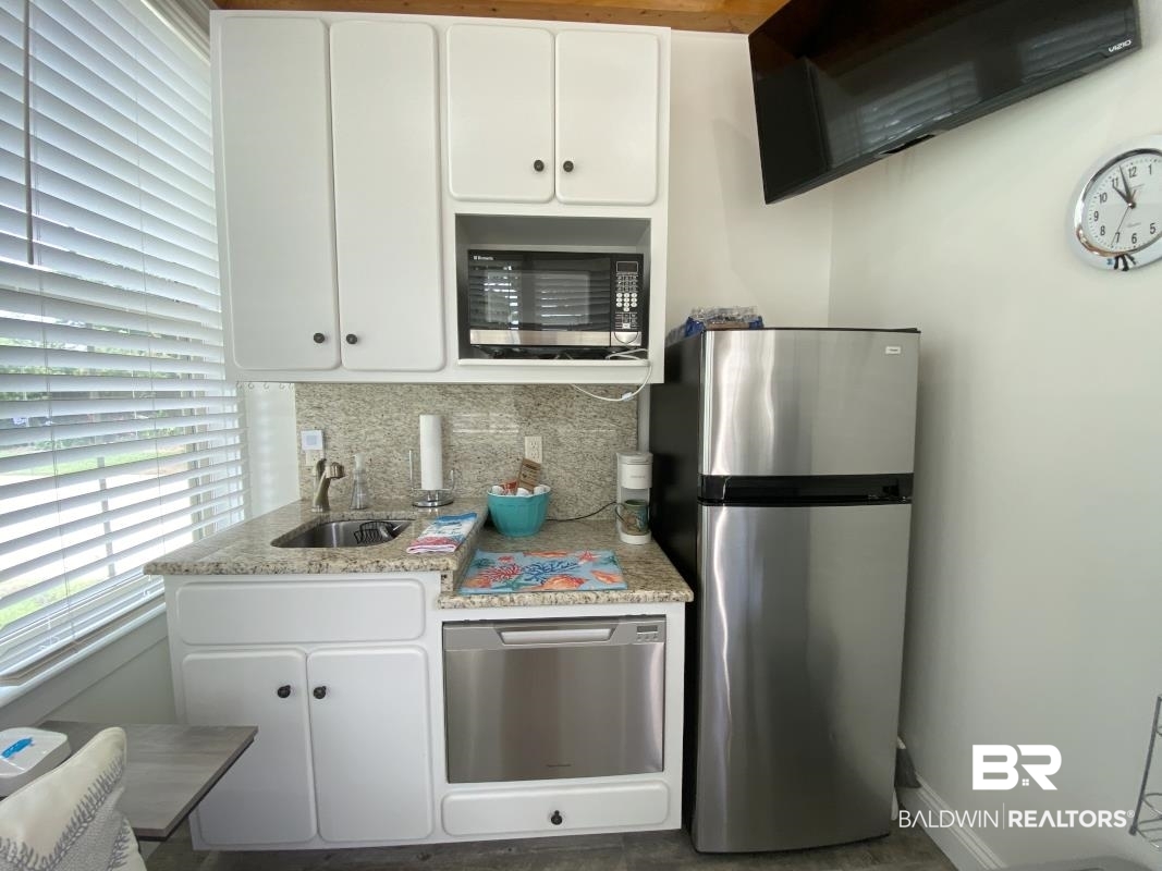 28888 Canal Road, Unit 77 Orange Beach, AL 36561 - Photo 3 of 23 Compact kitchen with white cabinetry, granite-finish countertops, stainless steel sink, and stainless steel appliances including a refrigerator, microwave, and dishwasher