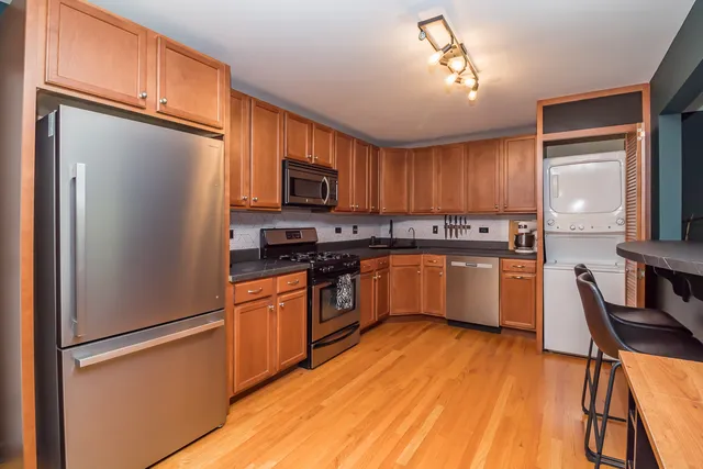 a kitchen with stainless steel appliances granite countertop white cabinets a refrigerator a stove a sink and dishwasher with wooden floor