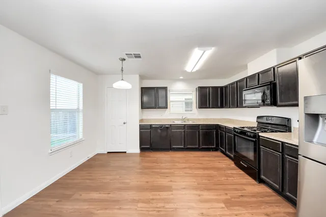 a large kitchen with stainless steel appliances granite countertop a large counter top a stove a sink dishwasher a refrigerator with grey cabinets and wooden floor