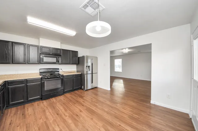 a kitchen with stainless steel appliances granite countertop a refrigerator a sink dishwasher a stove and white countertops with wooden floor