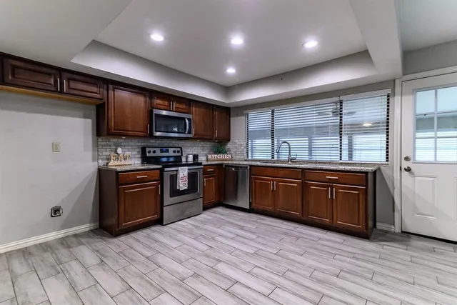 a kitchen with stainless steel appliances granite countertop wooden cabinets a stove a sink and a large window