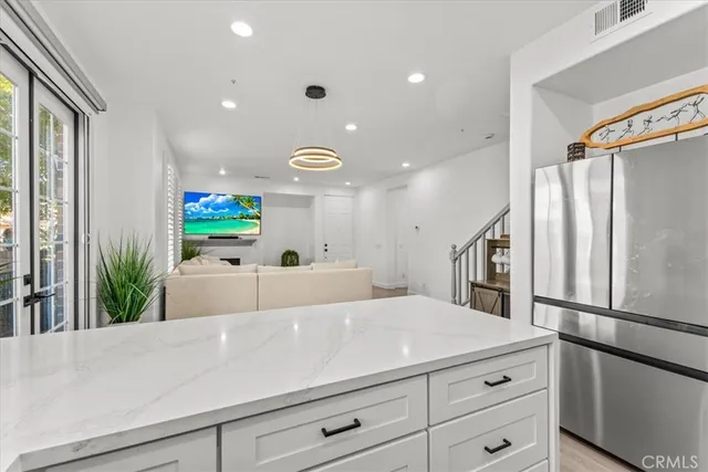 a living room with stainless steel appliances kitchen island granite countertop a refrigerator a sink and white cabinets next to a window