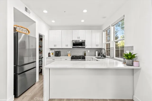 a kitchen with stainless steel appliances granite countertop a refrigerator a stove a sink a microwave and white cabinets with wooden floor