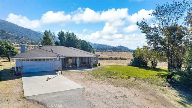 a view of a white house next to a yard with big trees and plants