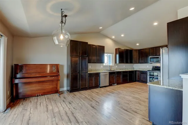 a kitchen with stainless steel appliances kitchen island granite countertop wooden floors wooden cabinets and chandelier