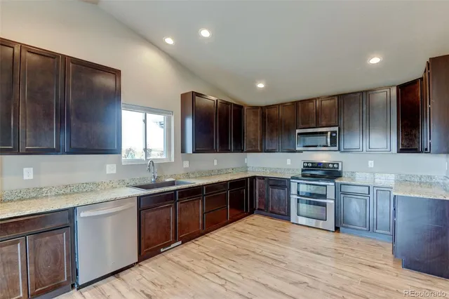 a kitchen with stainless steel appliances granite countertop wooden cabinets a sink dishwasher a stove and a refrigerator with wooden floor