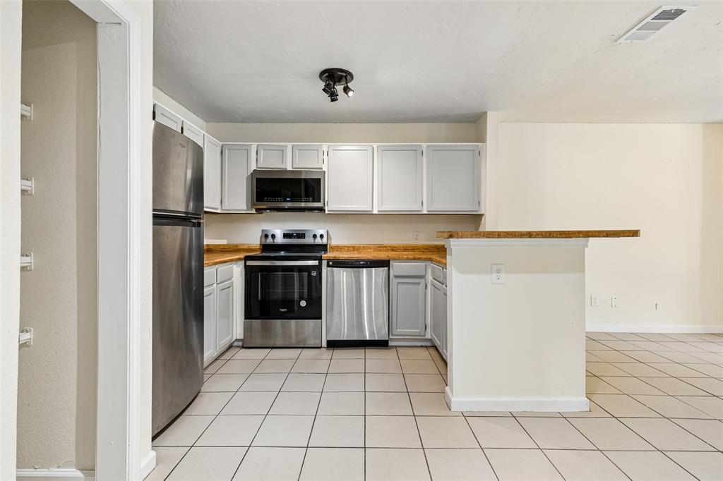 6108 Abrams Road, Unit 610 Dallas, TX 75231 - Photo 11 of 21 Kitchen featuring white cabinetry, stainless steel appliances, a bar-height countertop, and light-toned tile flooring